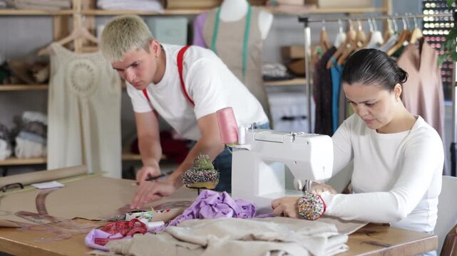 Team of tailors working in the workshop. Asian seamstress sewing clothes next to a guy fashion designer who draws patterns on paper. High quality 4k footage