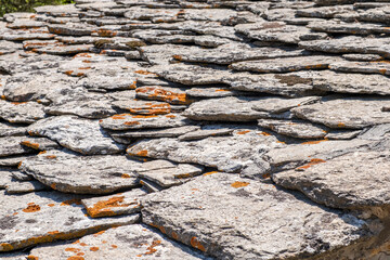 Sunlit layered stone roof with orange lichen