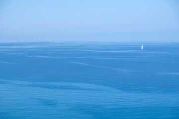 Solitary white sailboat upon calm blue sea horizon under clear daylight sky, minimal and serene