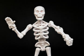 A small, articulated human skeleton model with red eyes, standing upright on a stark black background. Concepts of anatomy, biology, Halloween, fear, science, education, medical, spooky, and death.