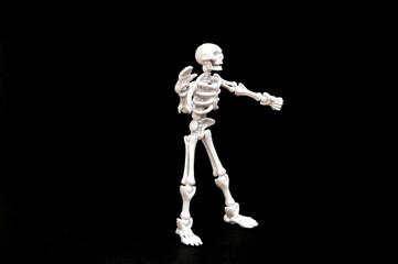 A small, articulated human skeleton model with red eyes, standing upright on a stark black background. Concepts of anatomy, biology, Halloween, fear, science, education, medical, spooky, and death.
