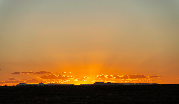 warm hues illuminate distant mountain ridges, serene sunset casting amber light across rolling hills