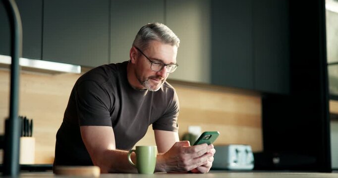 Mature man, phone and coffee in kitchen, texting and glasses for notification in morning at house. Person, smartphone and contact on mobile app, smile or scroll on social media with tea at apartment