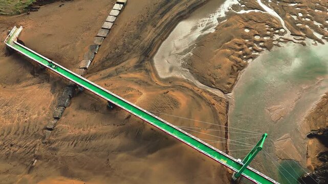mont&eacute;e progressive au dessus d'un pont en armature metallique et cables servant de passerelle entre deux plages. On y voit le sable humide de la mar&eacute;e basse ses dessins et une etendue d'eau