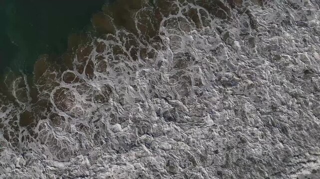 Vol vertical au dessus de l'&eacute;cume, la mousse m&eacute;lang&eacute; au sable  forme des dessins 