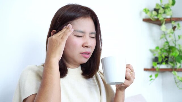 Asian woman experiencing a headache after drinking coffee,  effects of caffeine sensitivity and overconsumption and side effects.  stress, dehydration, and negative reactions to coffee