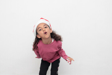 4-year-old Latina girl with curly brown hair wearing a santa hat sings with a candy cane to celebrate Christmas and New Year