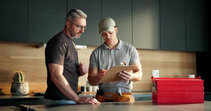 Mature man, plumber and talk with clipboard in kitchen, invoice or price for repair service in home. People, maintenance checklist and discussion with toolbox, sink and solution for leak at apartment