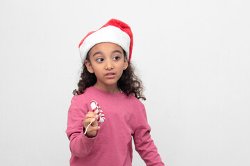 4-year-old Latina girl with curly brown hair wearing a santa hat sings with a candy cane to celebrate Christmas and New Year