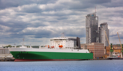 Fototapeta premium Large green and white cargo ferry docked in the harbor of Gdynia, Poland with Sea Towers in the background