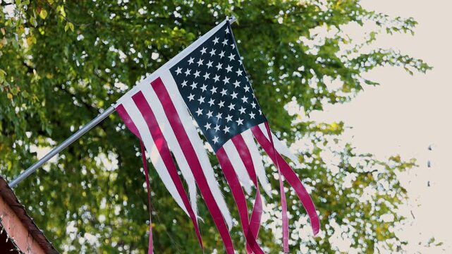 Worn American flag with torn stripes hanging from pole in afternoon light