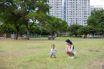 Baby walking on grass with mother at park