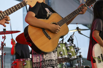 Fototapeta premium Energetic musician playing an acoustic guitar on stage during live music concert. band performs with passion at festival, with drums and another guitar in background
