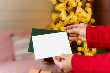 woman holds a New Year's card mockup in front of a sparkling Christmas tree