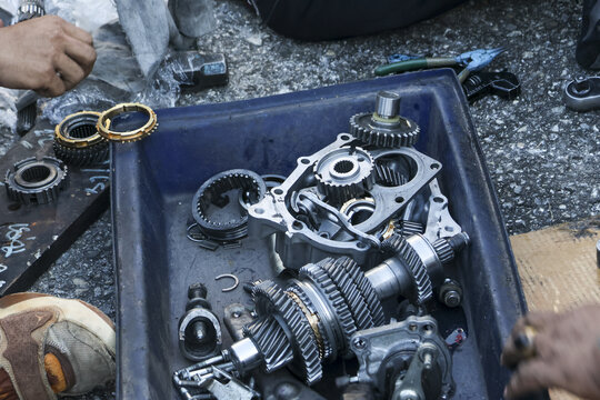 Focused mechanic working on complex automotive gearbox repair, with disassembled transmission gears and parts laid out during maintenance service - Powered by Adobe
