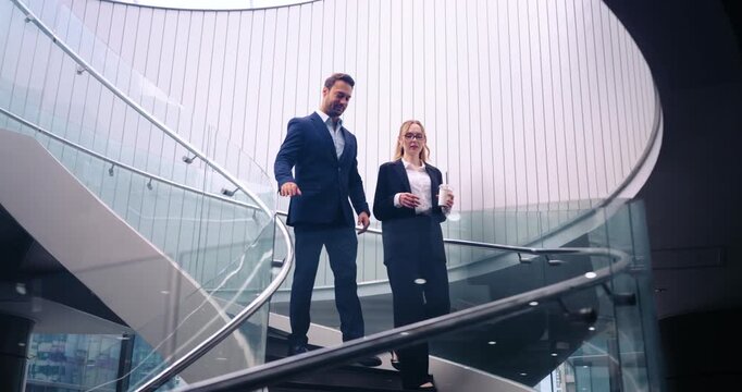 Businessman And a Businesswoman Holding A Cup Descend A Modern Staircase With Glass Railings. - wide shot