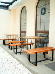 Outdoor seating area, outdoor cafe table with wooden bench top and black metal frame, beside wide glass window