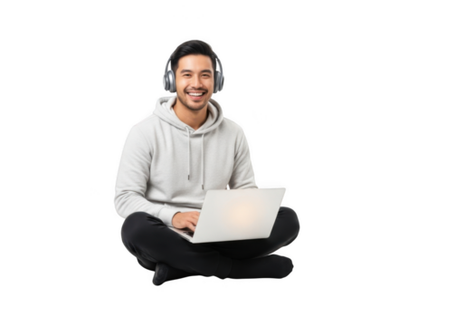 Smiling young man with headphones and laptop sitting cross legged on a plain surface isolated on transparent background
