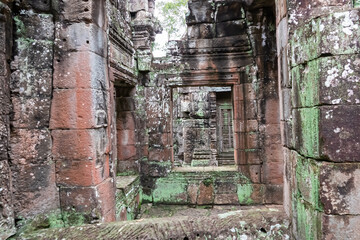 The view through a series of crumbling stone window frames creates a layered perspective, revealing the decaying yet beautiful interior of mysterious Khmer temple ruin in Angkor, Siem Reap, Cambodia.
