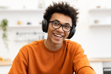 Fototapeta premium A young man with glasses and headphones smiles brightly at the camera, wearing an orange sweater.