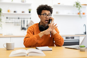 A young man wearing glasses is surprised while talking on his phone at home.