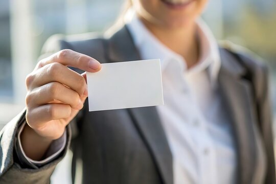 a professional businesswoman in a gray suit presents a blank white business card directly toward the viewer symbolizing networking and opportunity - Powered by Adobe