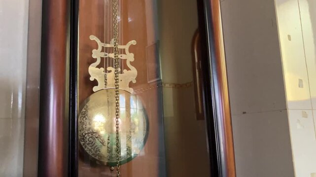 classic pendulum clock made of wood with a pendulum made of brass that swings left and right