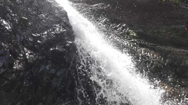 Slow motion low-angle shot at the base of Lipad Falls in Tabin Wildlife Reserve, showing water falling toward the camera and splashing into the pool in the Borneo jungle.