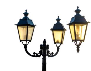 Close-up of three antique, ornate lanterns with glowing yellow lights, silhouetted against a stark black background