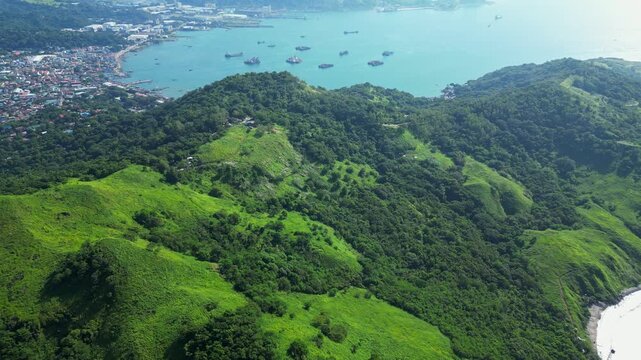 Elevated aerial of Nagbayog View Deck in Mariveles, Bataan, rising above lush green hills and winding paths to reveal the dramatic town coastline and calm turquoise sea below.