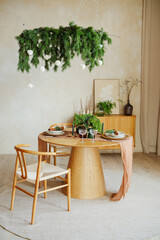 Festive dining table with green foliage chandelier and natural wood chairs in bright room