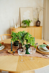 Table setting with green plants, candles and glassware on wooden table, warm interior decor