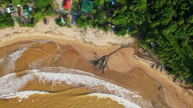 Higher top‑view aerial slowly rotating over the shoreline, highlighting black sand patterns and waves rolling onto the coast of Quinawan Beach in Mariveles, Bataan, Philippines.