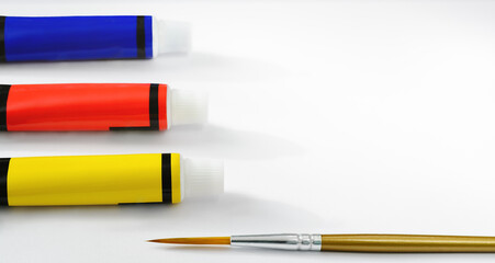 White background with yellow, red and blue paint tubes and a brush