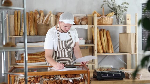 Man owner is busy checking paper documents, calculating income and expenses, expected increase in profit. Checks bill of lading. Bakery employee in apron examines documents, ponders debt restructuring