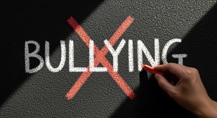 Hand drawing red cross over the word bullying on textured blackboard symbolizing anti bullying awareness education and stand against harassment