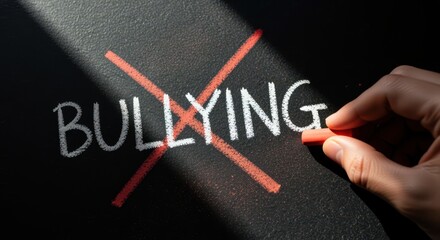 Hand crossing out the word bullying with red chalk on dark surface symbolizing anti bullying awareness prevention and social responsibility message