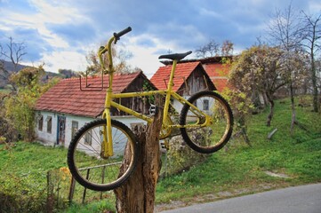 Old, rusty bicycle on the tree trunk in front of abandoned village