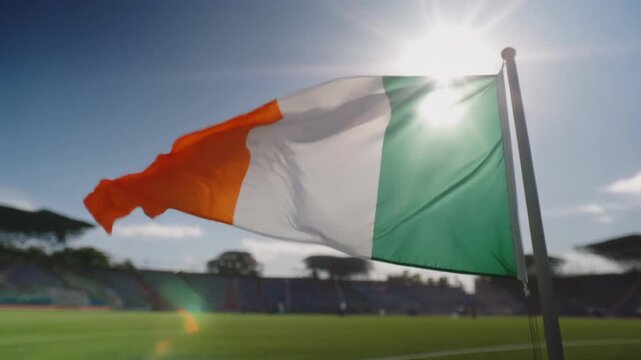 Dramatic close-up of Ivory Coast flag waving proudly at sunlit stadium event, capturing national pride and vibrant atmosphere