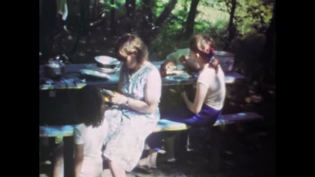 Family picnic in countryside outside city. Children, mother sharing meal together. Relaxation at picnic table outdoors in forest nature. Simple joys. Old film. Archival retro 1960s. Vintage archive