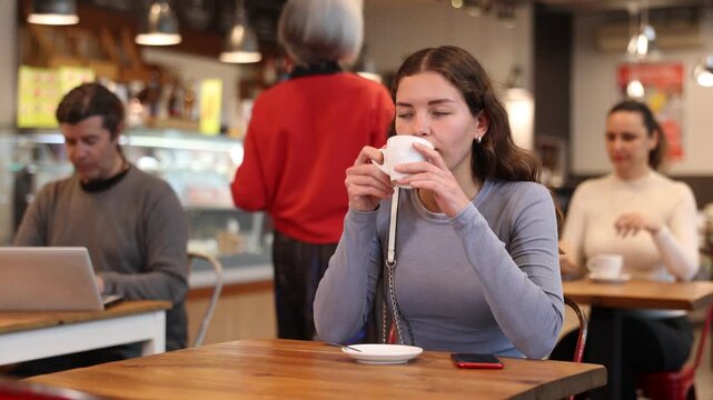 Cafe visitor drinks coffee alone. Girl whiles away time and waits for meeting in chain cafe, spend time while drinking coffee. 