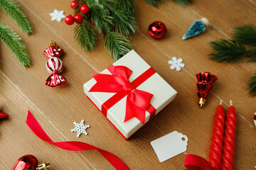 Gift box with red bow surrounded by festive Christmas ornaments and pine branches on wood