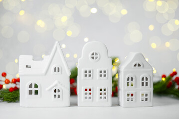 Three small white ceramic houses with Christmas decorations and soft bokeh lights in background
