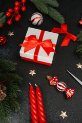 Festive gift box with red ribbon surrounded by evergreen branches, red berries, and candles.