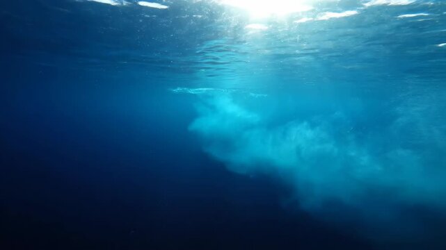 Underwater shot of clear blue water with sunbeams and sand cloud in the ocean.