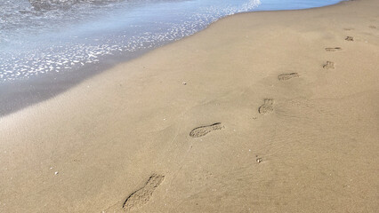 Footprints stretch along the sandy beach, a fleeting record of someone’s walk by the sea.
