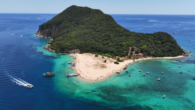 Aerial drone cinematic video of scenic caves and turquoise beach in paradise island of Marathonisi in bay of Laganas, visited by small boats a true tourist attraction, Zakithnos island, Ionian, Greece