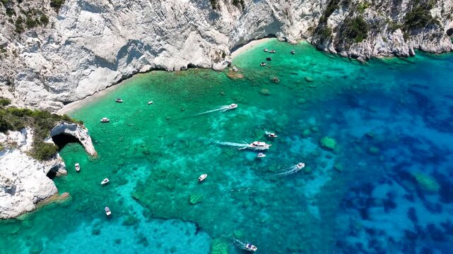 Aerial drone cinematic video of amazing white rock sea caves forming a blue lagoon visited by tour speed boats in small turtle island of Marathonisi, Zakinthos island, Ionian, Greece