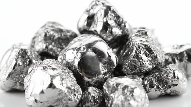 A close up shot of a pile of shiny silver nuggets displayed on a seamless white surface, reflecting soft light that captures its metallic texture.