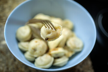 Close-up of a golden fork picking up a seasoned pelmeni or dumpling from a blue bowl, ready to be eaten as a comfort meal